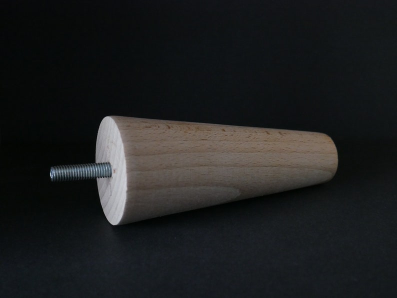 May include: A wooden furniture leg with a tapered design and a metal screw. The leg is light brown and has a smooth finish.