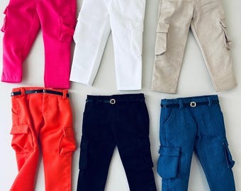 May include: Six pairs of doll-sized cargo pants in various colors: hot pink, white, tan, orange, black, and denim blue. Each pair features a black belt and side cargo pockets. The pants are displayed on a white surface.