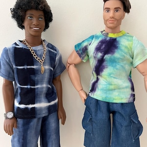Puede incluir: Dos mu&ntilde;ecos de pie uno al lado del otro. El mu&ntilde;eco de la izquierda tiene el pelo oscuro y rizado, una camiseta tie-dye azul y blanca, pantalones cortos a juego, un collar de cadena dorada y un reloj. El de la derecha tiene pelo casta&ntilde;o, una camiseta tie-dye verde, azul y morada y pantalones cortos cargo azules.