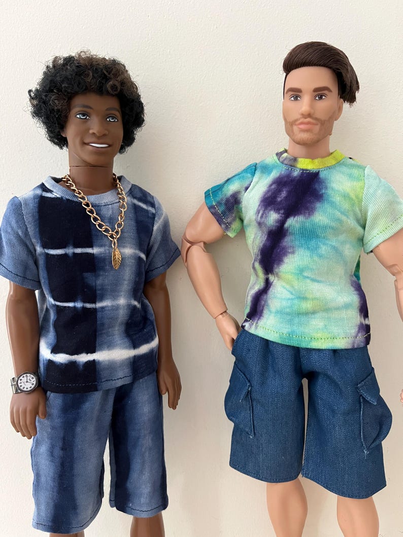 Puede incluir: Dos mu&ntilde;ecos de pie uno al lado del otro. El mu&ntilde;eco de la izquierda tiene el pelo oscuro y rizado, una camiseta tie-dye azul y blanca, pantalones cortos a juego, un collar de cadena dorada y un reloj. El de la derecha tiene pelo casta&ntilde;o, una camiseta tie-dye verde, azul y morada y pantalones cortos cargo azules.