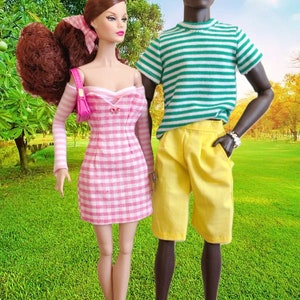 Puede incluir: Dos mu&ntilde;ecas de moda de pie juntas. La mu&ntilde;eca de la izquierda tiene el pelo casta&ntilde;o rojizo, un vestido de hombros descubiertos con cuadros vichy rosas y blancos, y un peque&ntilde;o bolso rosa. La mu&ntilde;eca de la derecha lleva una camiseta de rayas verdes y blancas, pantalones cortos amarillos y sandalias.
