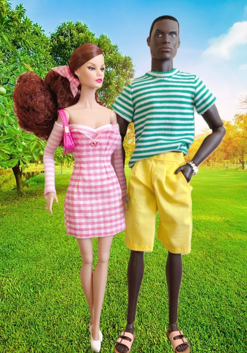 Puede incluir: Dos mu&ntilde;ecas de moda de pie juntas. La mu&ntilde;eca de la izquierda tiene el pelo casta&ntilde;o rojizo, un vestido de hombros descubiertos con cuadros vichy rosas y blancos, y un peque&ntilde;o bolso rosa. La mu&ntilde;eca de la derecha lleva una camiseta de rayas verdes y blancas, pantalones cortos amarillos y sandalias.