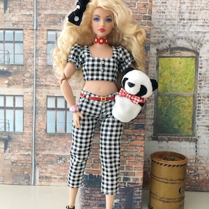 May include: A blonde doll wearing a black and white gingham crop top and matching capri pants, a red and white polka dot choker, a black and white polka dot hair bow, a pink wristwatch, and black shoes, holding a small plush panda with a red gingham bow.