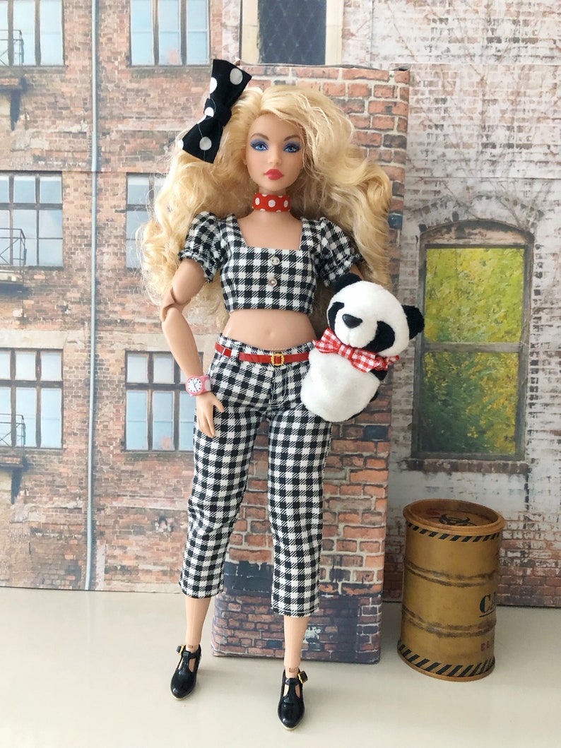 May include: A blonde doll wearing a black and white gingham crop top and matching capri pants, a red and white polka dot choker, a black and white polka dot hair bow, a pink wristwatch, and black shoes, holding a small plush panda with a red gingham bow.