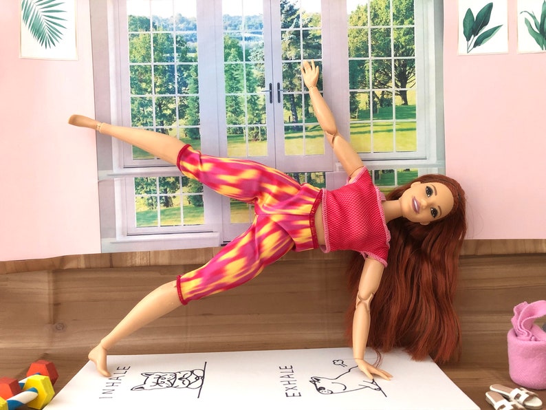 May include: A red and yellow patterned yoga outfit with a red tank top. The doll is in a yoga pose with the text "inhale" and "exhale" on the mat.