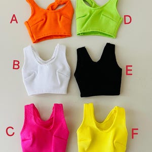 May include: Six sleeveless crop tops in various colors labeled A through F. The tops are orange, white, black, neon green, hot pink, and yellow. Each top features a scoop neckline, ribbed texture, and stitched bust detailing on the front.