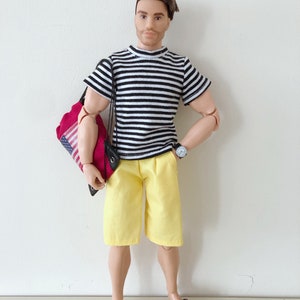 Puede incluir: Un mu&ntilde;eco con cabello casta&ntilde;o y barba que viste una camiseta a rayas blancas y negras, pantalones cortos amarillos y sandalias rosas. El mu&ntilde;eco lleva un reloj de pulsera negro en la mu&ntilde;eca izquierda y una bolsa roja con la bandera de EE. UU.
