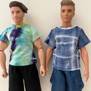 Puede incluir: Dos mu&ntilde;ecos articulados de pie uno al lado del otro. El mu&ntilde;eco de la izquierda tiene el pelo casta&ntilde;o y viste una camiseta tie-dye en verde, azul y morado con pantalones cortos negros. El de la derecha tiene el pelo casta&ntilde;o claro y viste una camiseta tie-dye azul y blanca con pantalones cortos cargo azules.