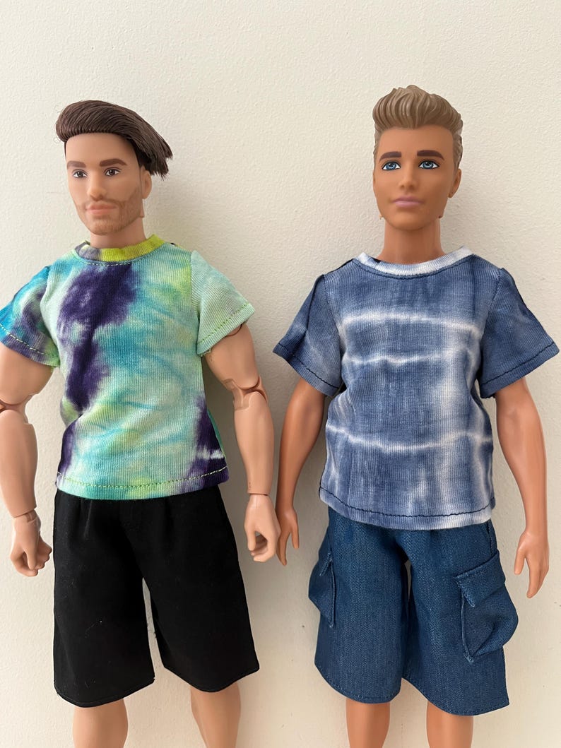 Puede incluir: Dos mu&ntilde;ecos articulados de pie uno al lado del otro. El mu&ntilde;eco de la izquierda tiene el pelo casta&ntilde;o y viste una camiseta tie-dye en verde, azul y morado con pantalones cortos negros. El de la derecha tiene el pelo casta&ntilde;o claro y viste una camiseta tie-dye azul y blanca con pantalones cortos cargo azules.