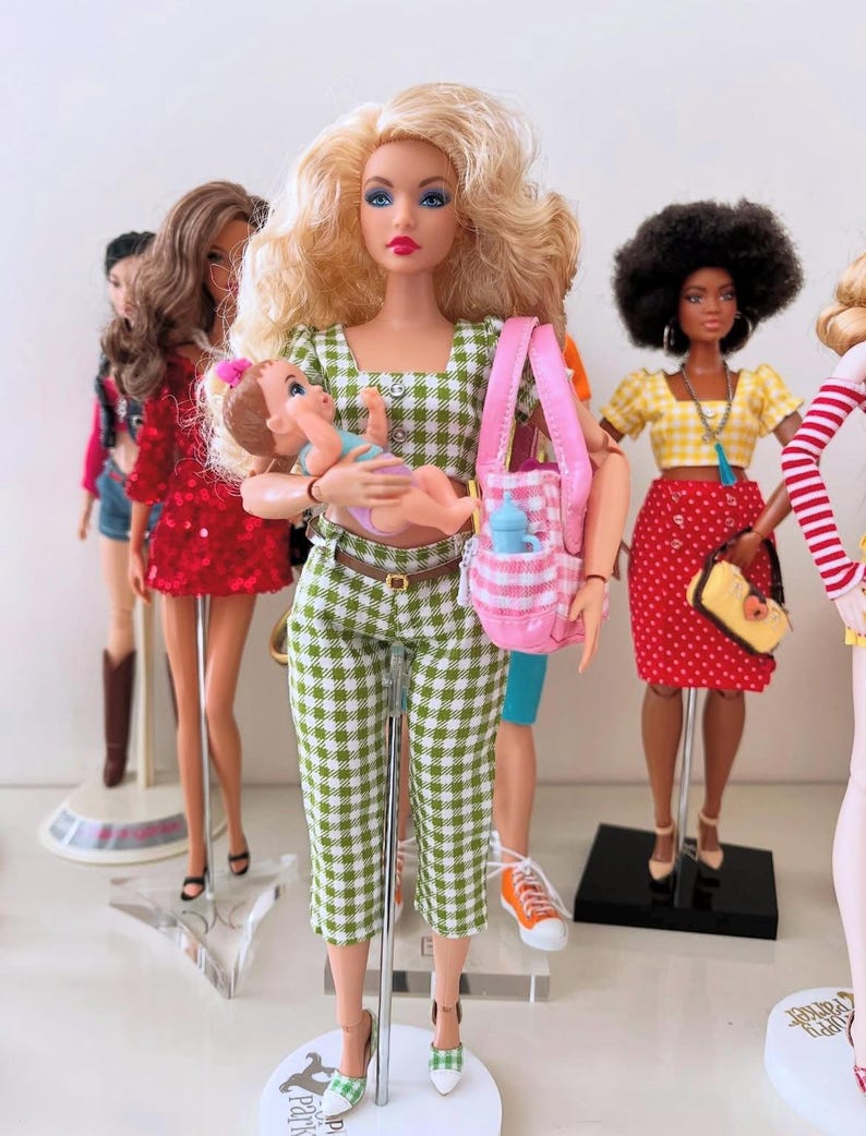 May include: A blonde doll wearing a green and white gingham crop top and matching capri pants, holding a small baby doll. The doll carries a pink and white checkered tote bag containing a blue bottle, standing among other dolls in various outfits.