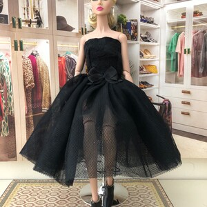 以下が含まれることがあります： 黒いストラップレスのドレスは、チュールスカートとウエストに黒いリボンが付いています。ドレスは、ブロンドの髪と青い目のファッションドールが着用しています。ドールは黒いヒールブーツを履いています。