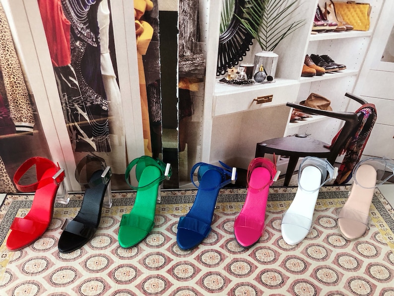 Op de afbeelding: Zeven paar sandalen met hoge hakken en doorzichtige hakken. De sandalen zijn in verschillende kleuren, waaronder rood, zwart, groen, blauw, roze, wit en nude.