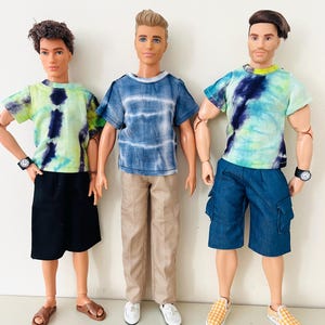 Puede incluir: Tres mu&ntilde;ecos masculinos de pie uno al lado del otro. El mu&ntilde;eco de la izquierda lleva una camiseta tie-dye verde lima y azul marino, pantalones cortos negros y sandalias marrones. El mu&ntilde;eco central lleva una camiseta tie-dye azul, pantalones beige y zapatos blancos. El mu&ntilde;eco de la derecha lleva una camiseta tie-dye verde lima y azul marino, pantalones cortos cargo azules y zapatos sin cordones a cuadros amarillos.