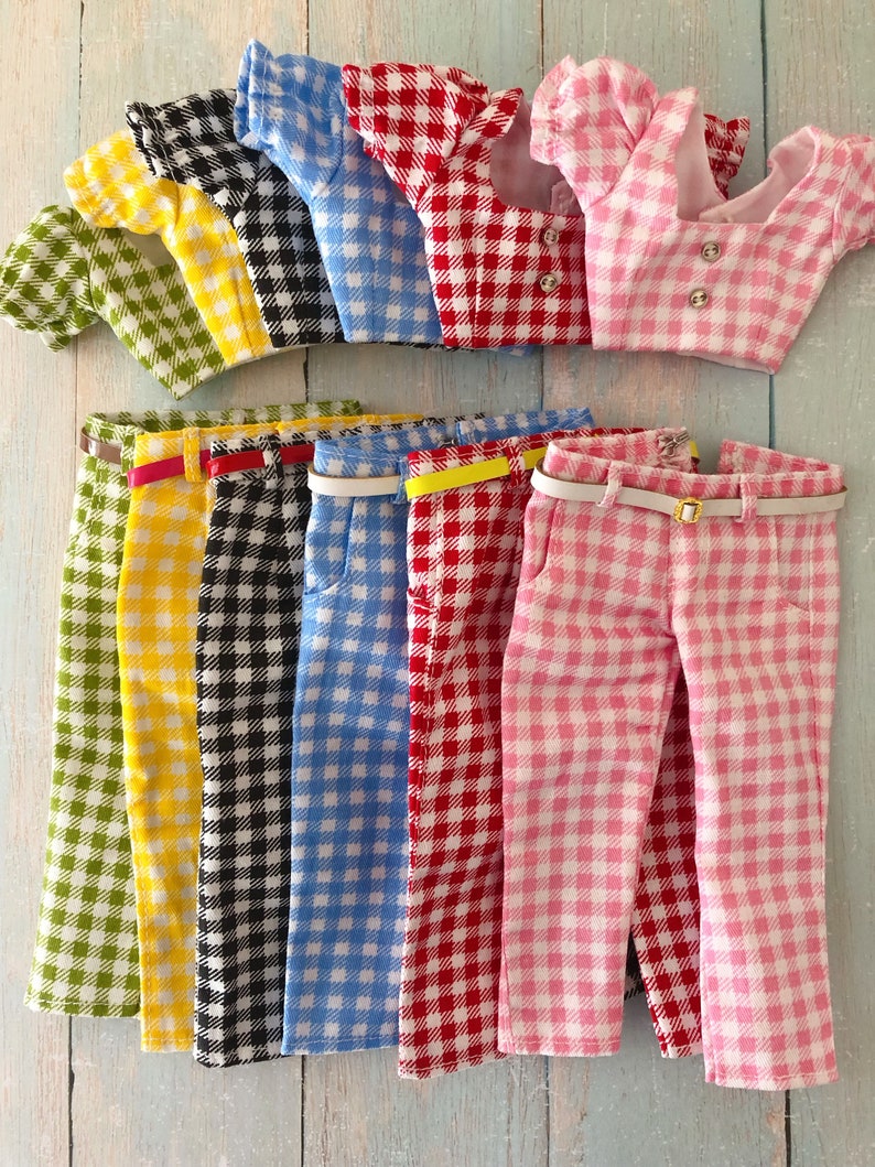 May include: A collection of six doll outfits, each consisting of a short-sleeved blouse and matching trousers in a gingham check pattern. The sets come in green, yellow, black, blue, red, and pink, with each pair of trousers featuring a thin belt.