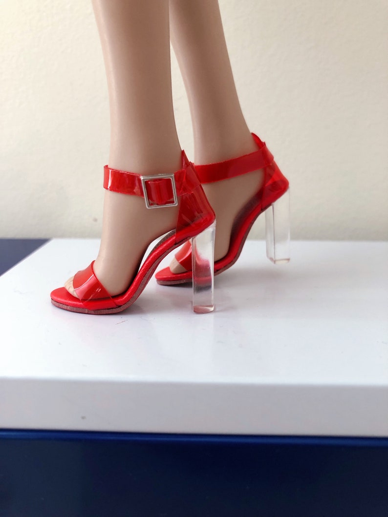 Op de afbeelding: Rode sandalen met hoge hakken, met doorzichtige acryl hakken en een gespsluiting.