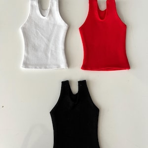 May include: Three sleeveless tank tops in solid colors: one white, one red, and one black. Each tank top features a scoop neckline and a straight hemline, designed as miniature apparel for dolls or small figures with a simple, clean construction.
