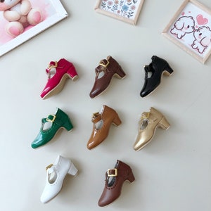 May include: Eight pairs of miniature doll shoes in various colors, including red, brown, green, gold, white, and black. Each shoe has a gold buckle and a small heel.