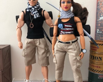 May include: Two fashion dolls wearing casual outfits and carrying backpacks. The male doll is wearing a black tank top, khaki shorts, sunglasses, and a black and white scarf. The female doll is wearing a black tank top with an American flag design, khaki cargo pants, and a gray scarf. Both dolls are holding a sword in each hand.