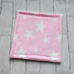 May include: A pink fleece blanket with white stars. The blanket is soft and cosy, perfect for snuggling up on the sofa.