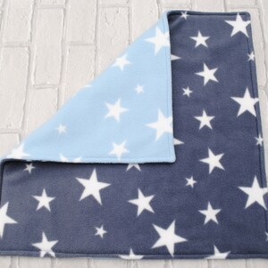 May include: A soft, reversible baby blanket with a blue side featuring white stars and a navy blue side featuring white stars.