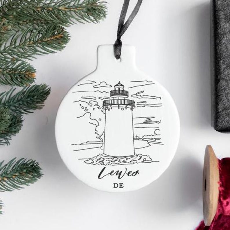 Peut inclure: Ornement en c&eacute;ramique blanche avec un dessin au trait noir d'un phare et le texte "Lewes DE".