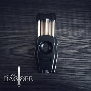 May include: A black cigar cutter with a silver blade and a silver knob. The cutter is shaped like a dagger and has the words "CIGAR DAGGER" printed on the bottom.