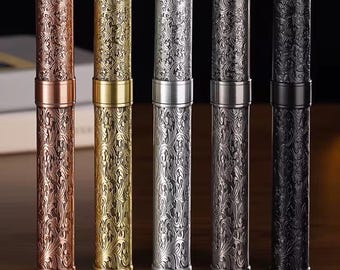 May include: Five metal pen holders in varying colors: copper, gold, silver, gunmetal, and black. Each cylindrical holder features an ornate, repeating floral pattern. The pen holders are displayed vertically against a dark background.