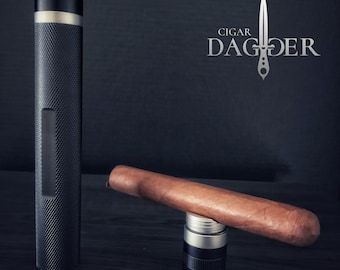 May include: A black metal cigar cutter with a textured surface and a silver band. The cutter is next to a brown cigar resting on a silver cigar holder.