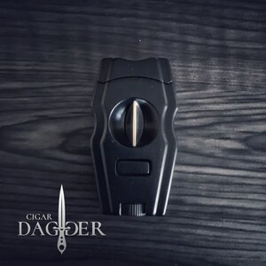 May include: Black cigar cutter with a gold blade and a silver logo that says "CIGAR DAGGER".