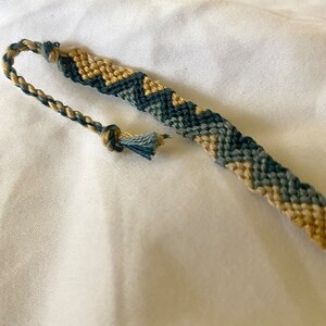 May include: A friendship bracelet with a chevron pattern in shades of blue and beige.