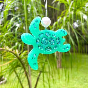 May include: A teal green glitter turtle ornament with a white pearl hanging from a white string.
