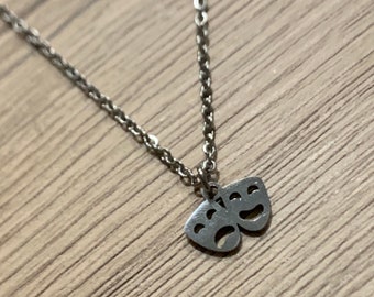 May include: A silver necklace with a small pendant featuring two theater masks, one smiling and one frowning.