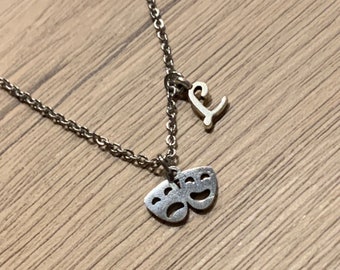 May include: A silver necklace with a charm of two theater masks and a letter 'L' charm.