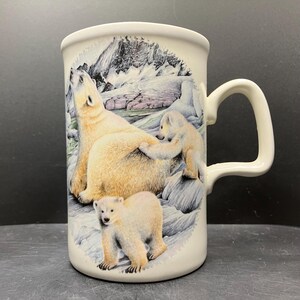 May include: White ceramic mug featuring a polar bear family scene. The design includes a large adult bear, two cubs, and a snowy mountain backdrop. The mug has a curved handle and a glossy finish, suitable for hot beverages.