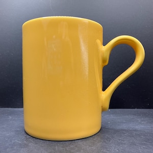 Peut inclure: Une tasse en céramique jaune uni avec une anse incurvée. La tasse a une forme cylindrique et une finition brillante. La poignée est également jaune.