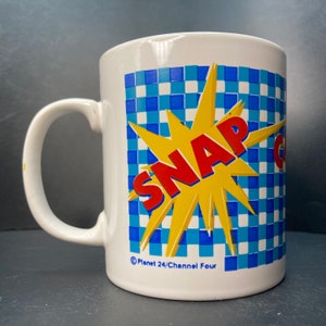 May include: White ceramic mug with a blue and yellow checkered pattern. The word "SNAP" is in red letters on a yellow starburst. The mug has a Planet 24/Channel Four logo.