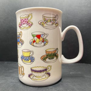 May include: White ceramic mug with a colorful teacup pattern. The mug has a handle and features various teacups with different designs and colors.