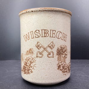 Peut inclure: Pot en céramique beige avec le mot "WISBECH" en lettres marron. En dessous, des clés croisées et des illustrations de bâtiments et d'arbres. Le bord et la base ont une bordure marron plus foncée.