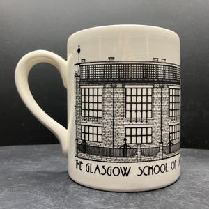May include: Cream ceramic mug with a black and white illustration of a building. The mug has a curved handle and the text "THE GLASGOW SCHOOL OF ART" is printed on the front. The mug is a standard size.