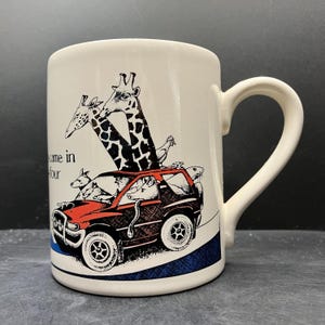 May include: Cream-coloured ceramic mug featuring a cartoon illustration of animals in a red and black SUV, including giraffes, kangaroos, and a snake. The mug has a curved handle and the text "came in four".
