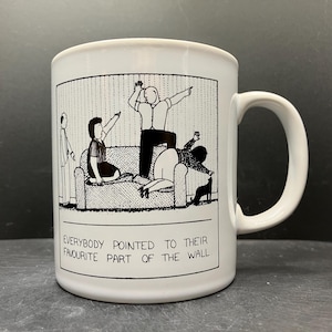 Peut inclure: Mug en céramique blanche avec une illustration de dessin animé en noir et blanc de personnes pointant vers un mur. Le texte sur la tasse se lit comme suit : « TOUT LE MONDE A INDIQUÉ SA PARTIE PRÉFÉRÉE DU MUR. »