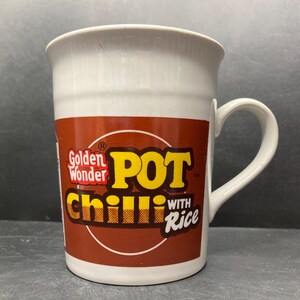 May include: White ceramic mug with a brown and yellow logo that says "Golden Wonder POT Chilli with Rice".