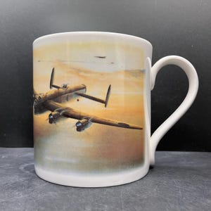 May include: White ceramic mug featuring a detailed illustration of a vintage airplane in flight against a sunset sky. The mug has a curved handle and a glossy finish, perfect for coffee or tea.