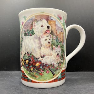 May include: White ceramic mug with a colourful illustration of three West Highland White Terriers, a bagpipe, and a castle. The mug has a red and green plaid pattern at the base and rim. The handle is white.