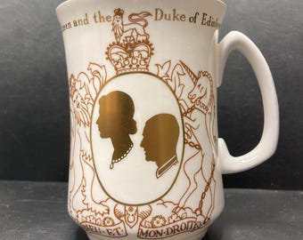 May include: White ceramic mug with a gold design featuring a royal crest, the text "Queen and the Duke of Edinburgh", and the text "Dieu et Mon Droit".