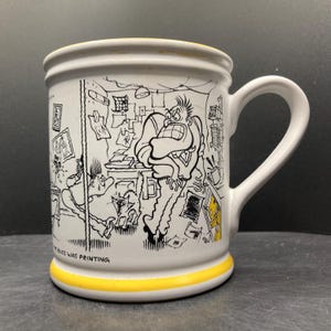 Könnte beinhalten: Weiße Keramiktasse mit gelbem Boden und Rand, mit einer schwarz-weißen Cartoon-Illustration einer Büroszene. Die Illustration zeigt eine gestresste Person, die von Papierkram umgeben ist. Die Tasse hat einen gebogenen Griff.