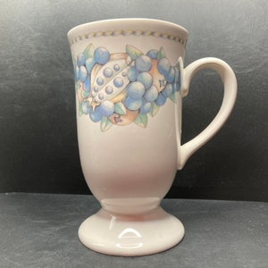 Könnte beinhalten: Weiße Keramiktasse mit Fuß. Die Tasse hat ein blaues und gelbes Blumenmuster mit einem Fruchtmotiv.