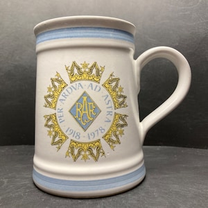 May include: A white ceramic mug with a blue and white stripe design around the top and bottom. The mug features a blue and gold emblem with the text "RAF" and the words "Per Ardua Ad Astra 1918-1978" in a circle around the emblem.