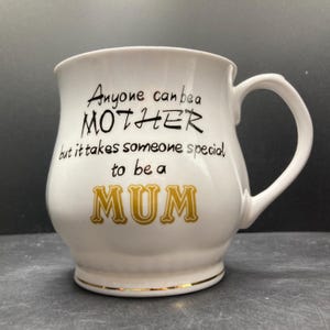 May include: White ceramic mug with a curved handle and a gold rim. The mug features the text "Anyone can be a MOTHER but it takes someone special to be a MUM" in black and gold lettering. A gift for Mother's Day.