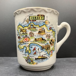 May include: Cream-colored ceramic mug featuring a map of Jersey with landmarks and text. The mug has a scalloped rim and a curved handle. The map includes the text "Jersey" and "English Channel".